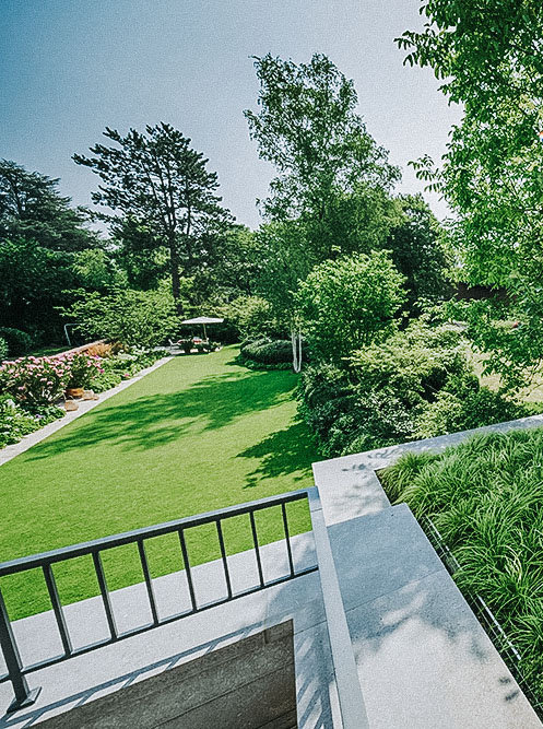 Balkon mit großer Kübelpflanzung und Blick auf den Privatgarten mit großer Rasenfläche und Staudenbeet