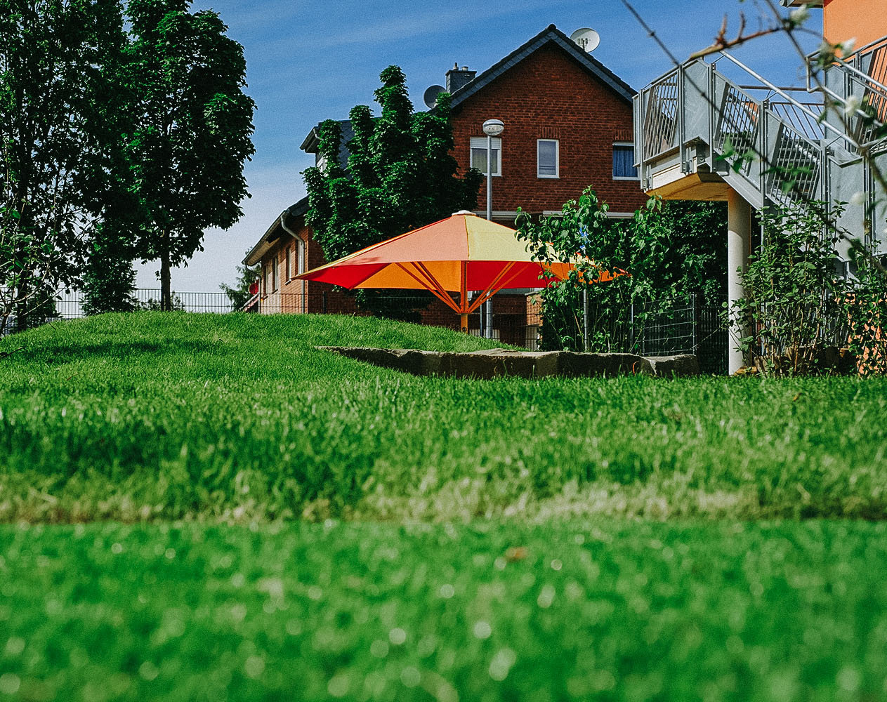Rasenfläche eines Kindergarten Außenbereichs mit Sonnenschirm
