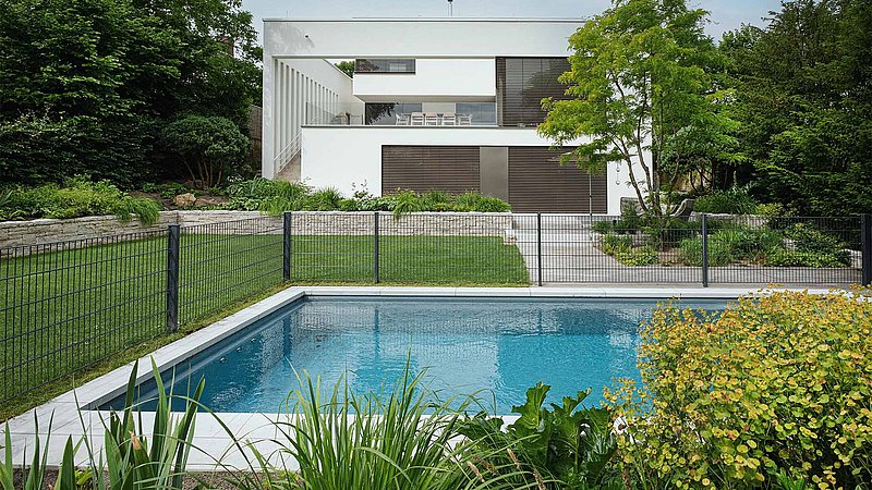 Blick von Pool auf Garten und Haus. Um den Pool befindet sich ein Zaun als Schutz.