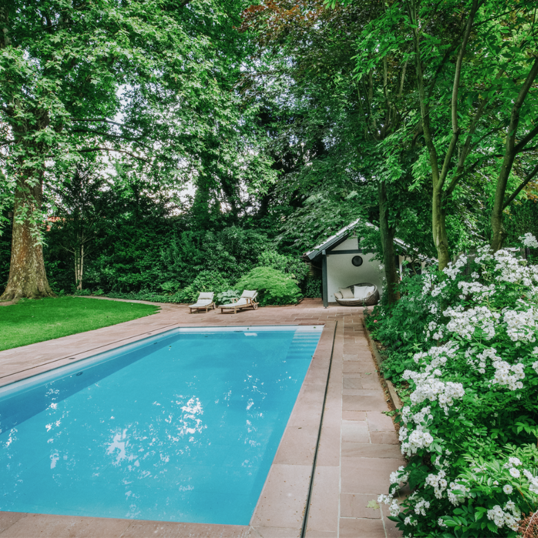 Ein langer Pool mit Natursteinplatten und Poolhaus in einem Garten