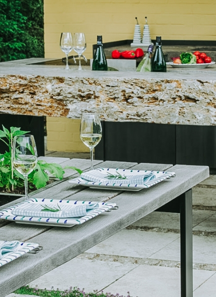 Gedeckter Tisch steht vor einer Outdoor-Küche aus Stein.