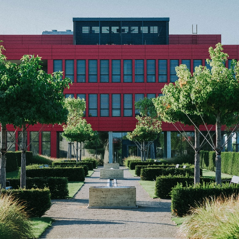 Moderne Grünanlage vor rotem Gewerbegebäude.