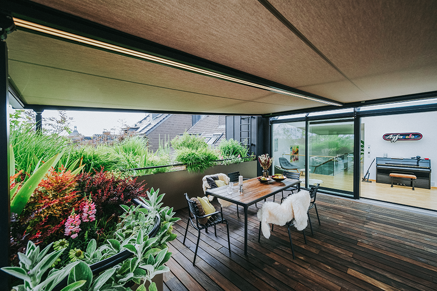Eine Dachterrasse mit Holzdielen aus Thermoeiche und üppig bepflanzten Beeten. Über der Terrasse befindet sich ein herausfahrbares Sonnendeck.