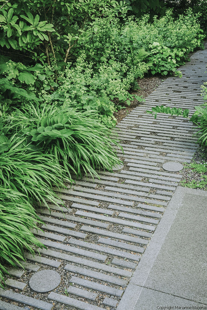 Ein aus kreis- und stäbchenform bestehender Gartenweg wird von üppiger grüner Bepflazung umgeben