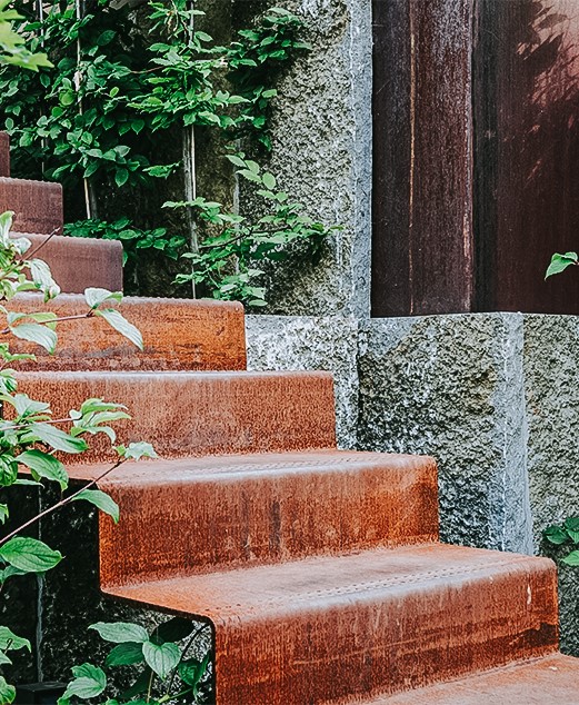 Eine Treppe aus Cortenstahl, die über Krustenplatten in einen Privatgarten in Alfter hinabführt